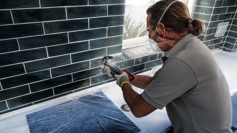 Người đeo thiết bị an toàn sử dụng dụng cụ điện để cắt gạch bên dưới cửa sổ.
