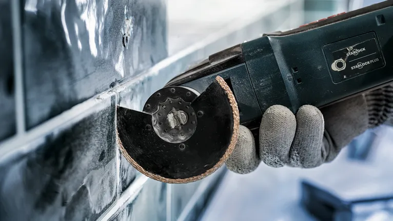 Một người mặc đồ bảo hộ đang sử dụng dụng cụ điện để cắt gạch.