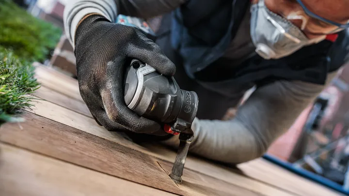 Người đeo thiết bị an toàn sử dụng dụng cụ điện để cắt tấm ván gỗ.