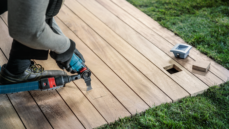 Người mặc đồ bảo hộ đang cắt sàn gỗ bằng dụng cụ điện.