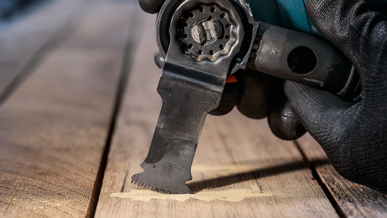 Người đeo thiết bị an toàn đang sử dụng dụng cụ đa năng để cắt gỗ.