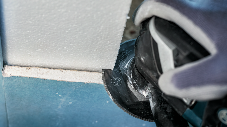 Người đeo thiết bị an toàn đang cắt tấm thạch cao bằng dụng cụ điện.