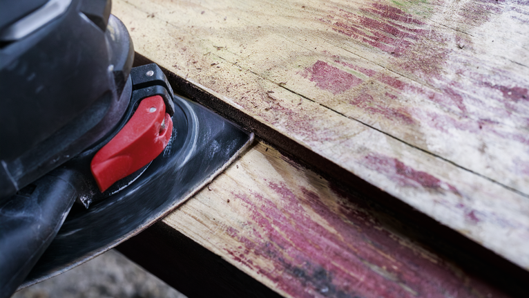 Máy chà nhám điện đang làm mịn tấm ván gỗ bị phong hóa.