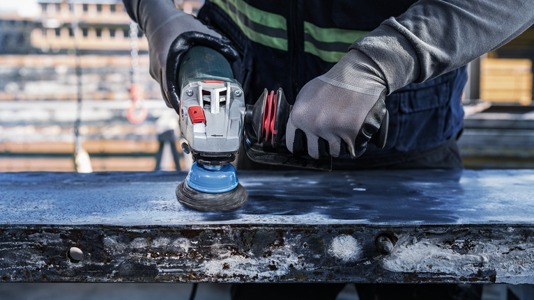 Người đeo thiết bị an toàn đánh bóng bề mặt kim loại bằng dụng cụ điện.