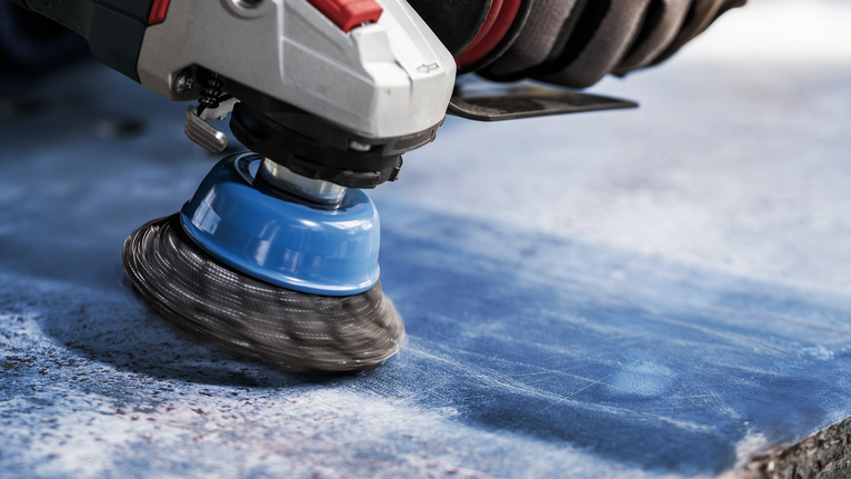 Người đeo thiết bị an toàn mài bề mặt đá xanh bằng bàn chải kim loại.