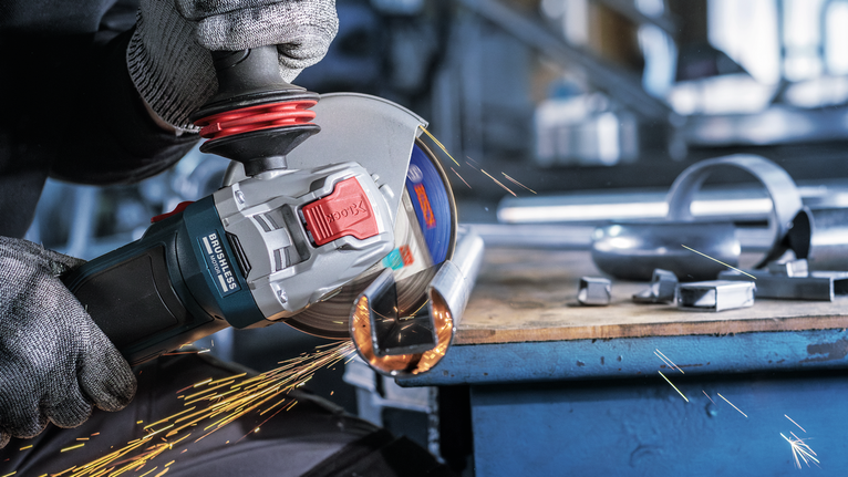 Một người mặc đồ bảo hộ mài một ống kim loại, tạo ra tia lửa.