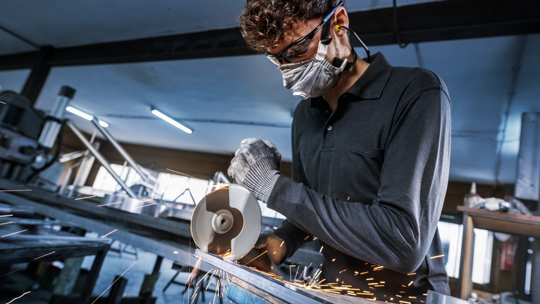 Người đeo thiết bị an toàn cắt kim loại bằng máy mài góc, tia lửa bắn ra.