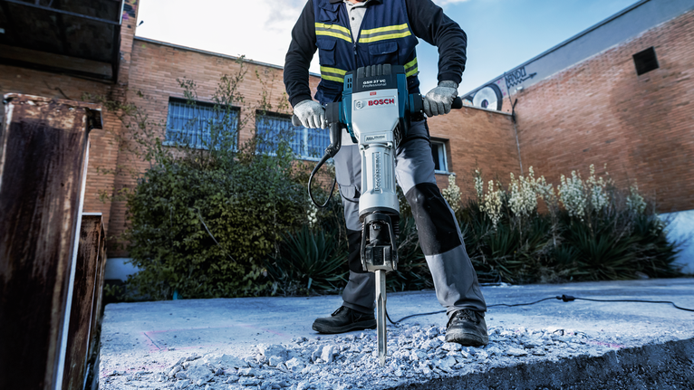 Một người mặc đồ bảo hộ sử dụng máy phá bê tông để phá dỡ bê tông ngoài trời.