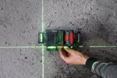 Một người đang điều chỉnh một thiết bị cân bằng laser chiếu những đường màu xanh lá cây lên sàn bê tông.