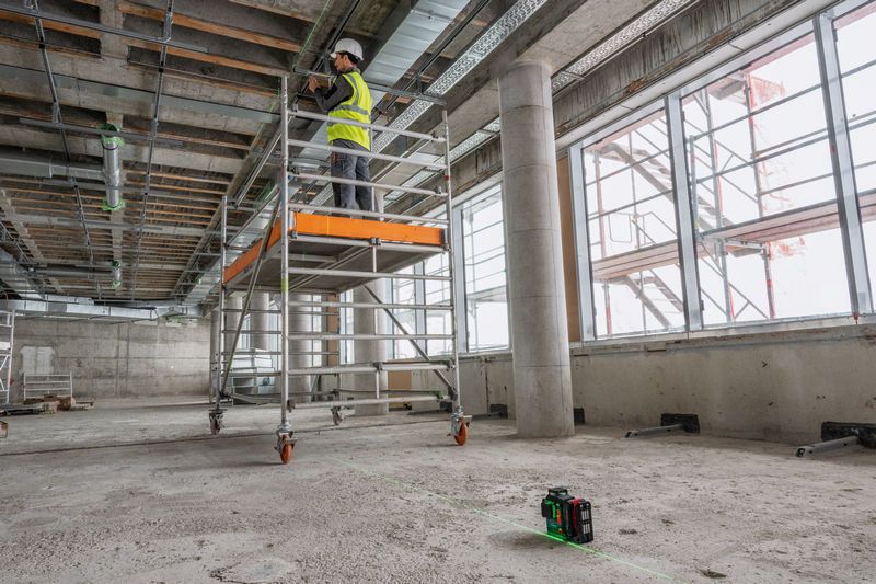 Một người mặc đồ bảo hộ đang làm việc trên giàn giáo, với một dụng cụ cân bằng laser chiếu các đường thẳng.