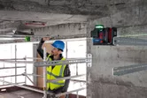 Một người đeo thiết bị an toàn đang căn chỉnh các thanh kim loại bằng dụng cụ cân bằng laser.