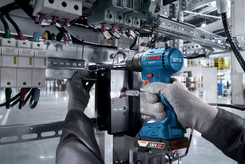 ISR 18V-30 P Một người mặc đồ bảo hộ đang sử dụng máy khoan không dây trên bảng điện.