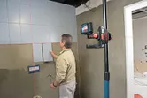 Một người đang căn chỉnh gạch ốp tường bằng dụng cụ cân bằng laser gắn trên một cây sào dài.