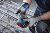 Người đeo thiết bị an toàn chuẩn bị sử dụng cờ lê lực không dây trên lưới kim loại.