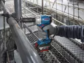 Một người mặc thiết bị an toàn đang sử dụng cờ lê lực không dây để mở một ống kim loại.