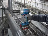 Một người mặc thiết bị an toàn đang sử dụng cờ lê lực không dây để mở một ống kim loại.