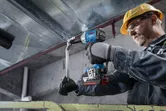 Một người mặc thiết bị an toàn đang siết chặt bu lông trên thanh kim loại bằng cờ lê lực không dây.