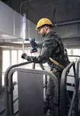 Một người mặc thiết bị an toàn đang sử dụng cờ lê tác động không dây trên hệ thống ống gió.