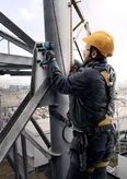 Một người mặc thiết bị an toàn sử dụng cờ lê tác động để vặn chặt bu lông trên kết cấu kim loại.