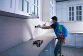 Người đang căn chỉnh tủ bếp bằng máy cân bằng laser trên giá ba chân.