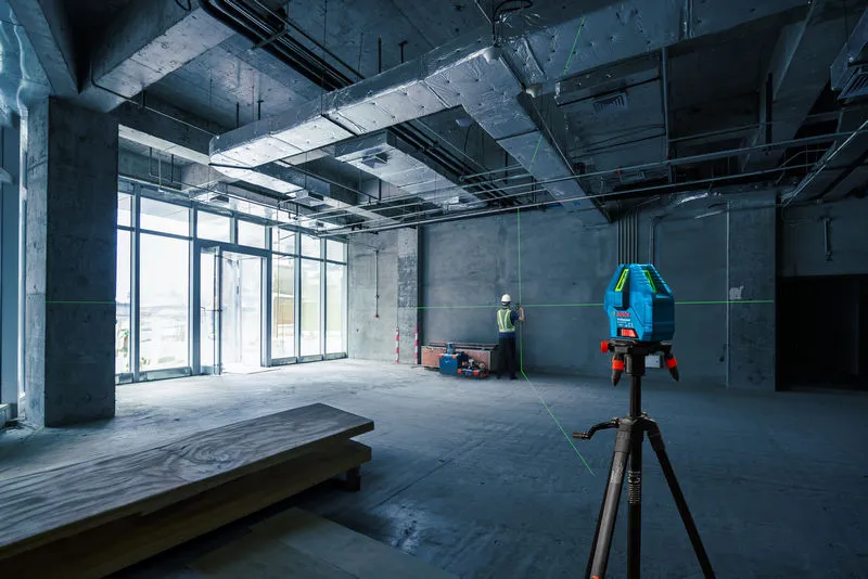 Một người mặc thiết bị an toàn đang căn chỉnh tường bằng máy cân bằng laser tại một công trường xây dựng.