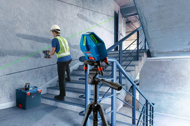 Một người mặc đồ bảo hộ đang khoan vào tường cầu thang bằng dụng cụ cân bằng laser.