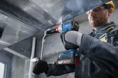 Một người mặc thiết bị an toàn sử dụng máy khoan không dây để cố định ống dẫn kim loại.
