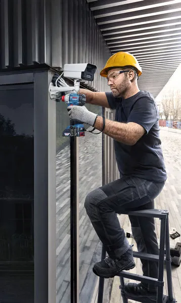 GDX 18V-285 Một người mặc thiết bị an toàn đang lắp đặt camera an ninh bằng máy khoan điện.