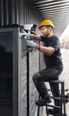 Một người mặc thiết bị an toàn đang lắp đặt camera an ninh bằng máy khoan điện.