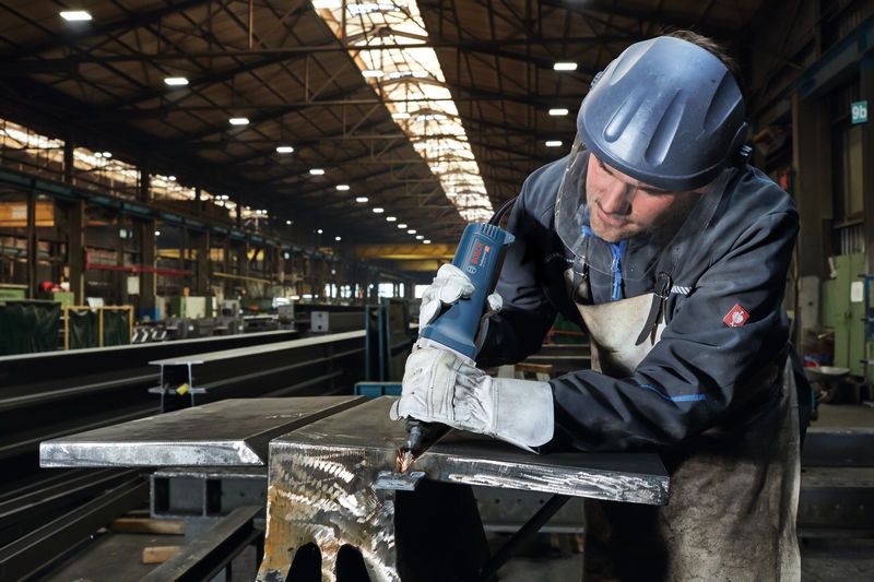 Một người mặc đồ bảo hộ sử dụng máy mài thẳng trên một thanh kim loại.