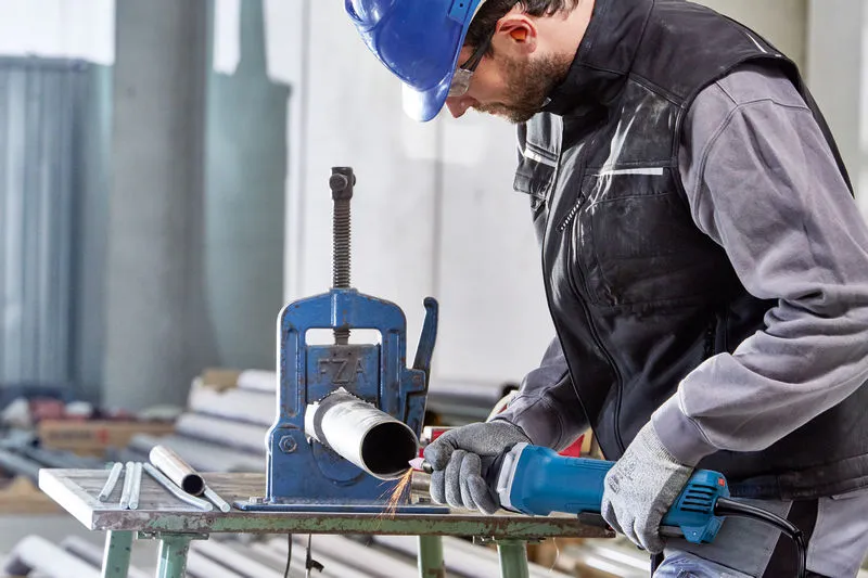 GGS 30 LPS Một người mặc đồ bảo hộ đang sử dụng máy mài thẳng để làm việc trên một ống kim loại.