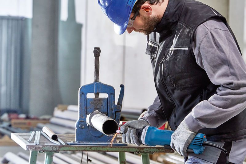 Một người mặc đồ bảo hộ đang sử dụng máy mài thẳng để làm việc trên một ống kim loại.