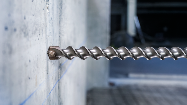 Mũi khoan xây lớn được lắp vào tường bê tông trong môi trường công nghiệp.