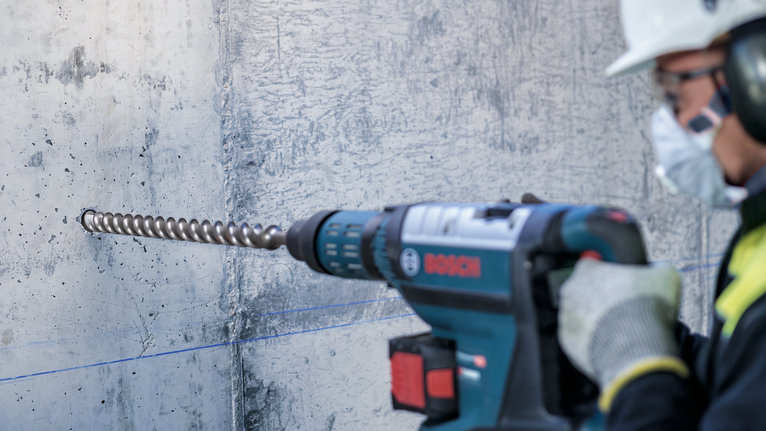 Một người mặc đồ bảo hộ đang khoan vào bức tường bê tông.