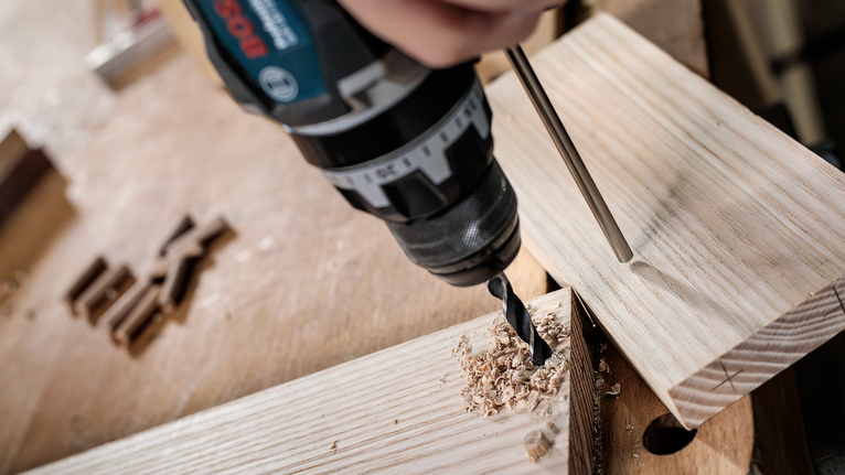 Bộ mũi khoan đầu đinh nhỏ PRO Wood, 7 chiếc Người đang khoan lỗ vào tấm ván gỗ trên bàn làm việc.