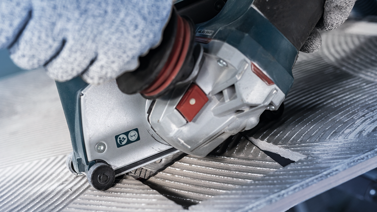 Người đeo thiết bị an toàn vận hành dụng cụ điện để cắt bề mặt kim loại có rãnh.