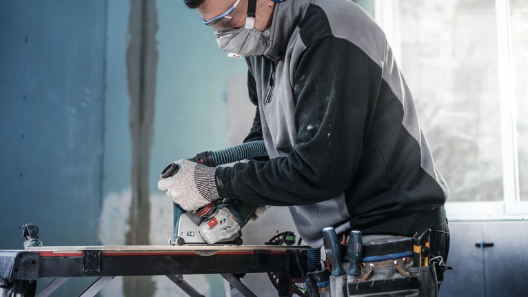 Người đeo thiết bị an toàn sử dụng cưa tròn để cắt gỗ trên bàn làm việc.