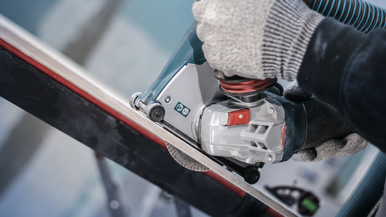 Người đeo thiết bị an toàn sử dụng dụng cụ điện để cắt thanh kim loại.