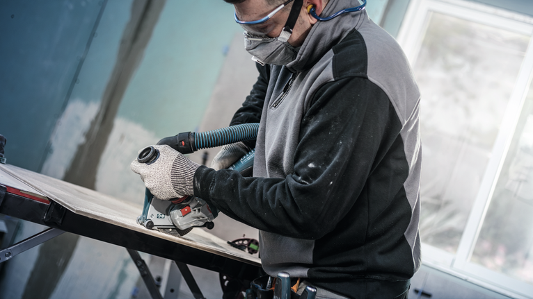 Người mặc đồ bảo hộ cắt gỗ bằng dụng cụ điện gắn vào ống hút bụi.