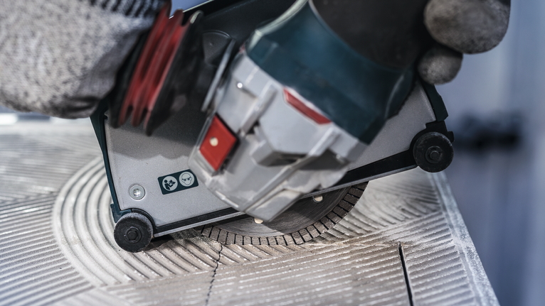 Người mặc đồ bảo hộ sử dụng máy cưa tròn để cắt gạch men.