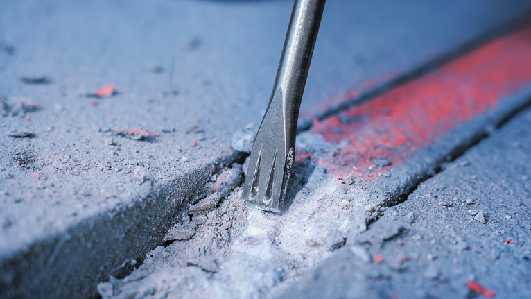 Mũi đục phá vỡ bê tông theo đường đã đánh dấu.