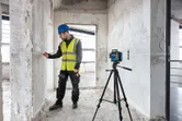 Một người mặc thiết bị an toàn đang đánh dấu tường bằng máy cân bằng laser trên chân máy xây dựng.