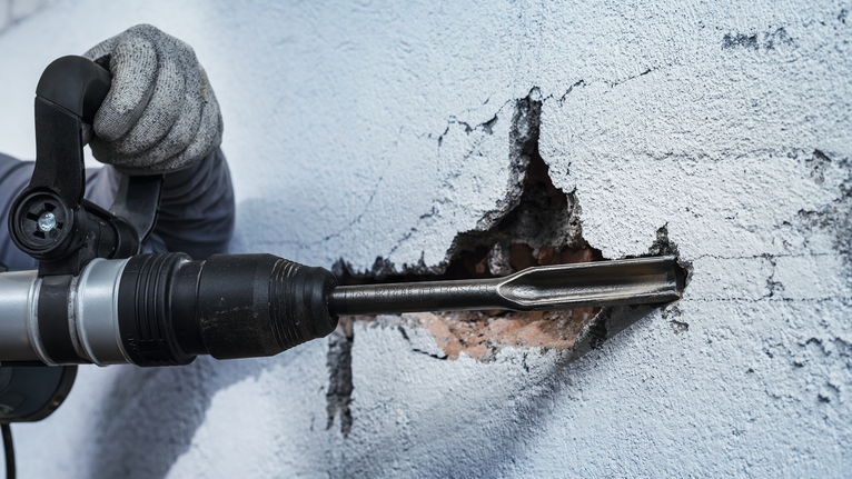 Một người mặc đồ bảo hộ sử dụng búa quay để đục vào tường.