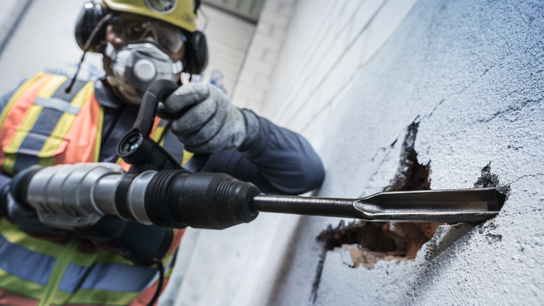 Người mặc thiết bị an toàn sử dụng búa quay để phá vỡ bức tường bê tông.