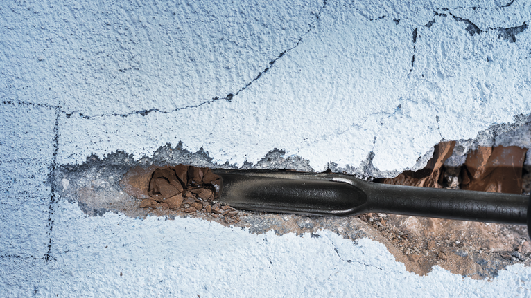 Dụng cụ đục phá vỡ lớp thạch cao trên bức tường đã sơn.