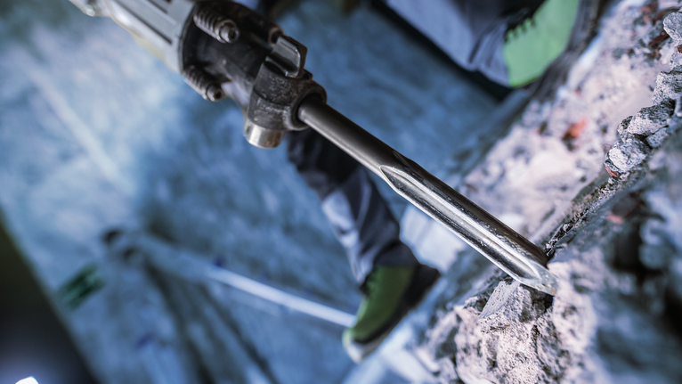 Người mặc đồ bảo hộ sử dụng búa phá dỡ để phá bê tông.