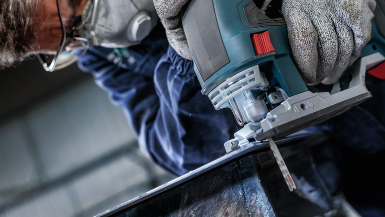 Người mặc đồ bảo hộ sử dụng máy cưa lọng để cắt kim loại.