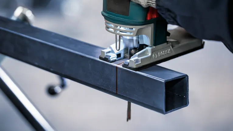 Người mặc đồ bảo hộ sử dụng máy cưa lọng để cắt một thanh kim loại.