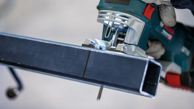 Người mặc đồ bảo hộ sử dụng máy cưa lọng để cắt một thanh kim loại.