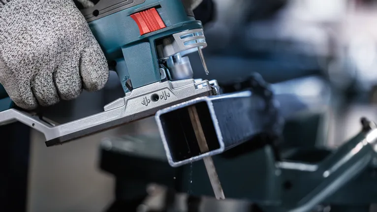 Người mặc đồ bảo hộ sử dụng máy cưa lọng để cắt một thanh kim loại.